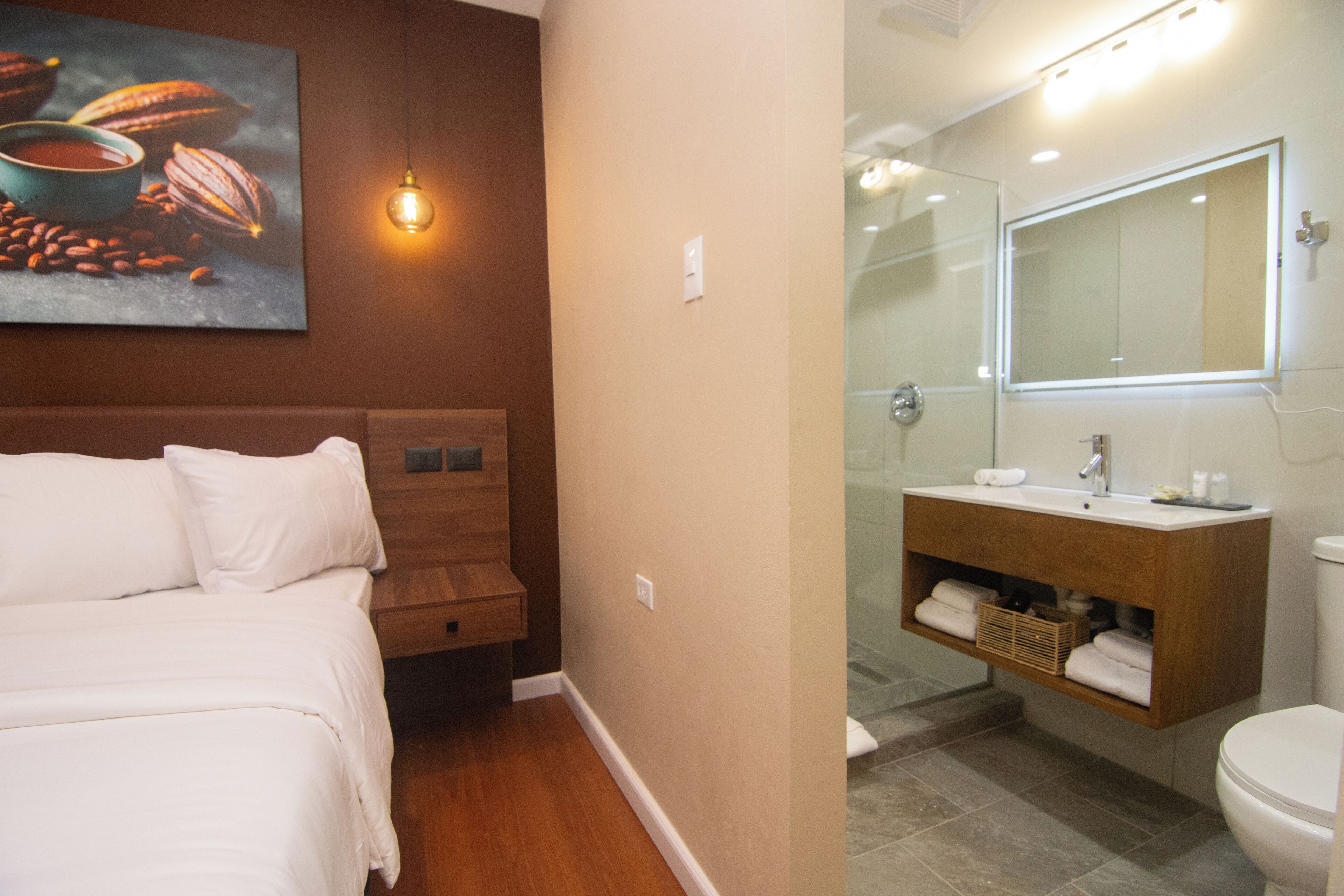 A hotel room with a bed, a wooden headboard, a bathroom with a mirror, sink, and shower.