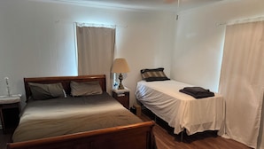 Ein Schlafzimmer mit einem hölzernen Bett, einem Einzelbett, einem Nachttisch mit Lampe und einem Fenster mit Vorhängen.