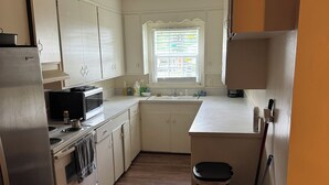 Eine Küche mit weißen Schränken, einem Edelstahl-Kühlschrank, einer Mikrowelle und einem Spülbecken.