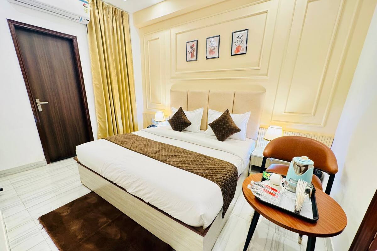 A hotel room with a bed, a bedside table with a lamp, a chair with a tray, and a door.