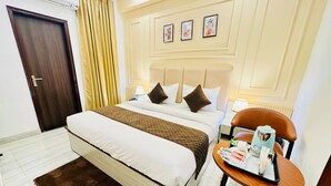 A hotel room with a bed, a bedside table with a lamp, a chair with a tray, and a door.