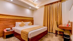 Habitación de hotel con cabecera de madera, cama con ropa de cama blanca, escritorio con silla y un ventanal con cortinas.