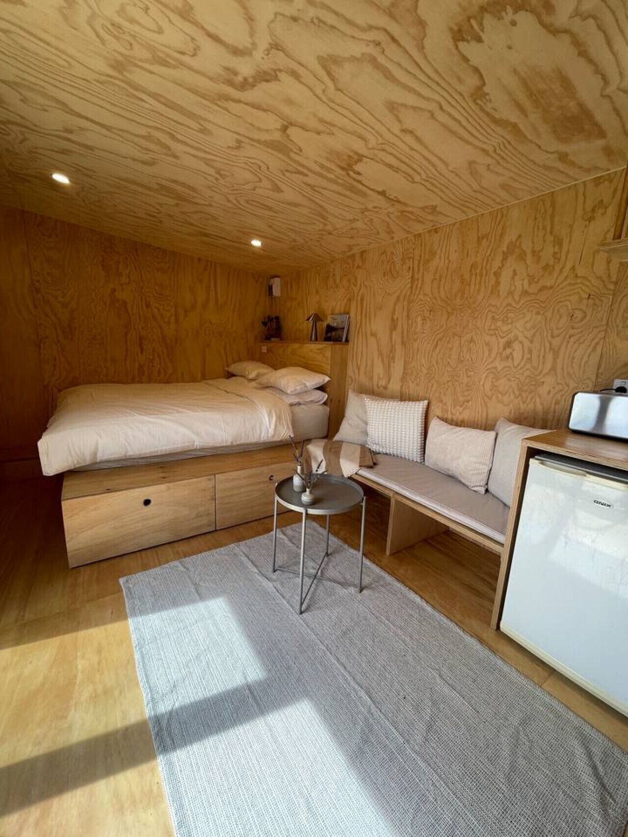 Een slaapkamer met een bed, een bank, een bijzettafeltje en een koelkast.