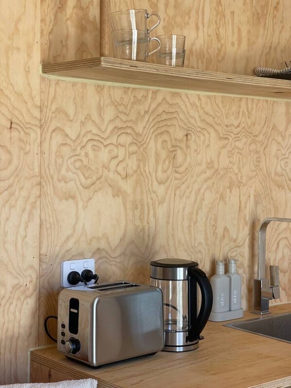 A kitchenette with a toaster, coffee maker, and glass mugs on a wooden shelf.