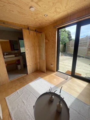 A modern interior with wooden walls, a sliding door leading to a garden, and a small table with decorative items. - Bastu Bicheno Tiny home (Bicheno)