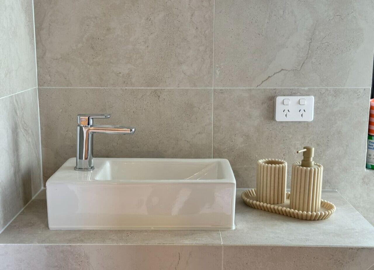 Un baño con un lavamanos rectangular, un grifo cromado, un perchero y un enchufe en la pared.