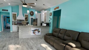 A spacious living area with a brown leather sofa, a kitchen with white cabinets, and a teal wall. - Coastal Comfort Retreat | Near Beach | Sleeps 10! (Rockport)