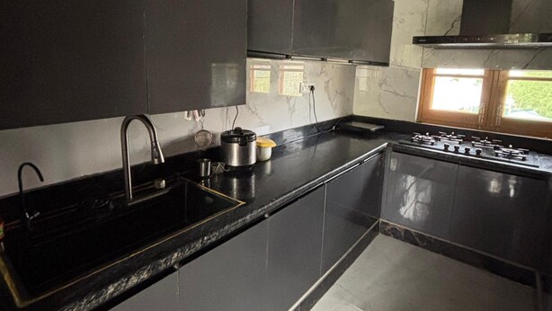 A modern kitchen with dark cabinetry, a stainless steel sink, and a gas stove. - Tranquil trails Naddi Mountain view (Dharamshala)