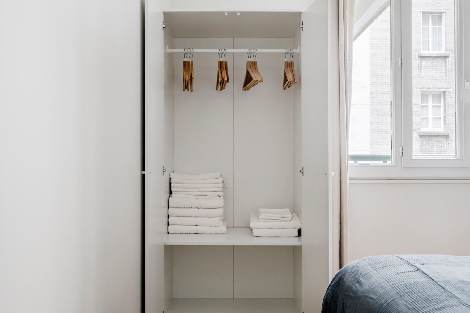 A white wardrobe with hanging clothes and folded towels.