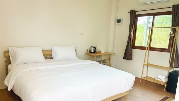 A bedroom with a large bed, a small table with a kettle, a shelf, and a window with curtains. - Nakai resort Sakon Nakhon (Sakon Nakhon)