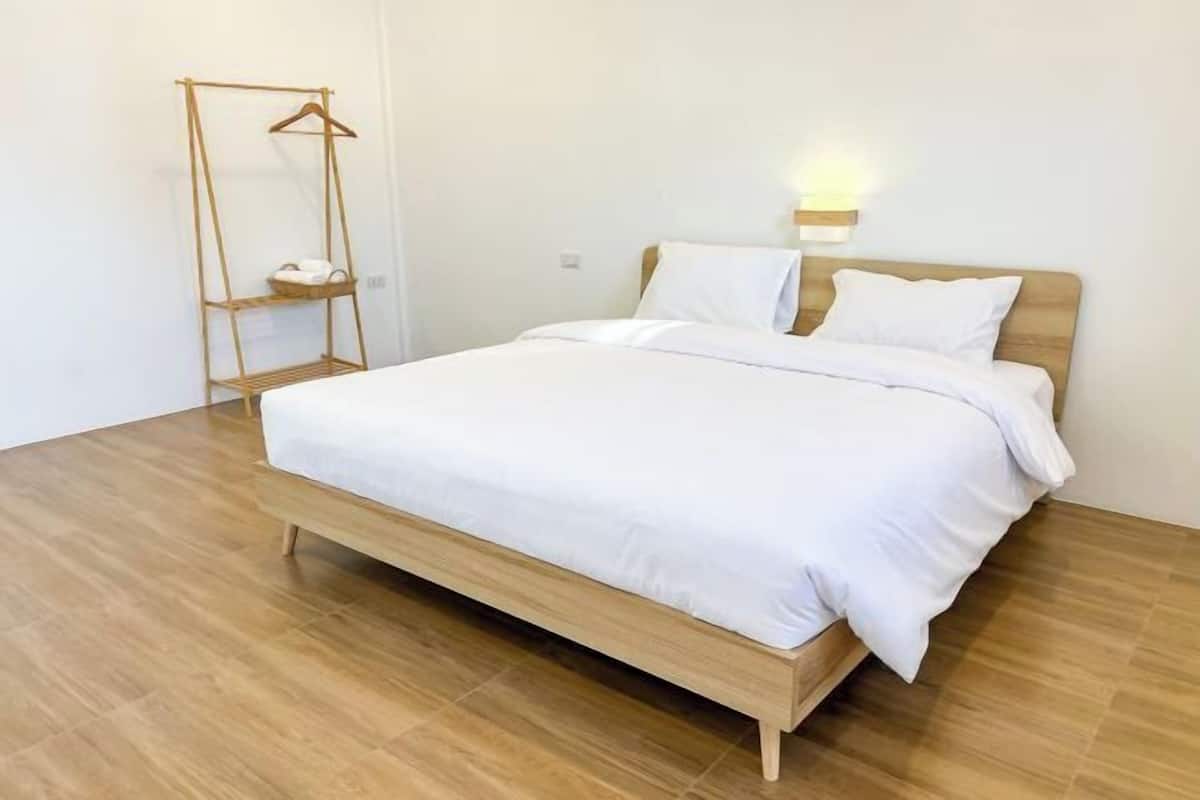 A single bed with a wooden frame, white bedding, a bedside table with a lamp, and a wooden floor.