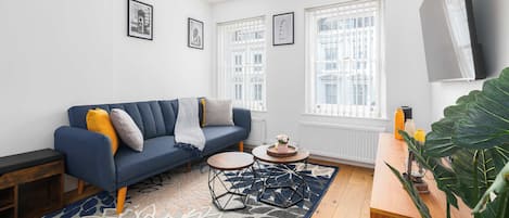 Una sala moderna con un sofá azul, una mesa de centro y una planta grande.