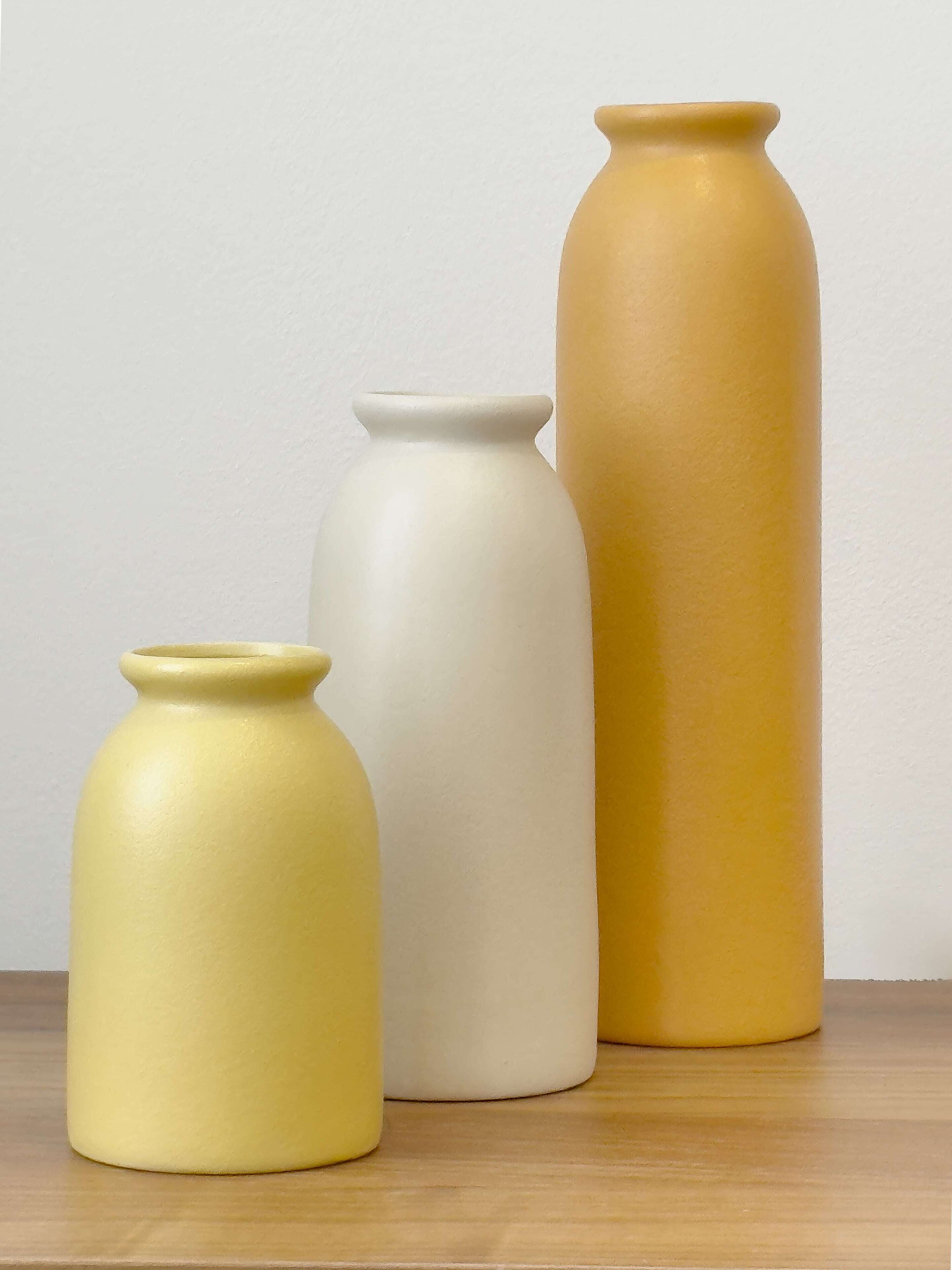 Three ceramic vases of varying sizes on a wooden surface against a plain wall.