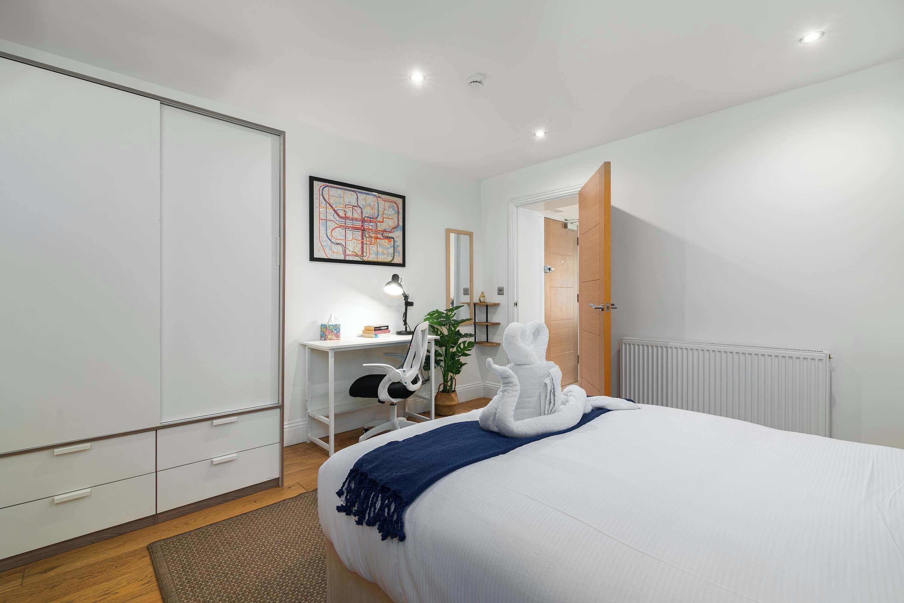 A bedroom with a bed, a desk, a chair, a map on the wall, and a radiator.