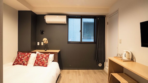 A hotel room with a bed, a desk, a window with curtains, and a wall-mounted air conditioner. - Tokyo Biyori Hotel (Tokyo)