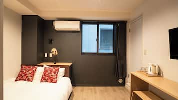 A hotel room with a bed, a desk, a window with curtains, and a wall-mounted air conditioner.