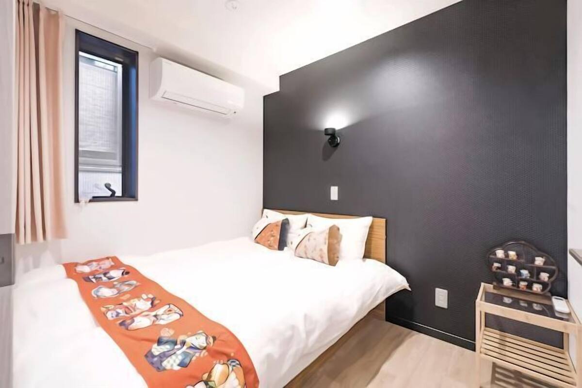 A bedroom with a bed, a bedside table, a wall-mounted light, and a window with curtains.