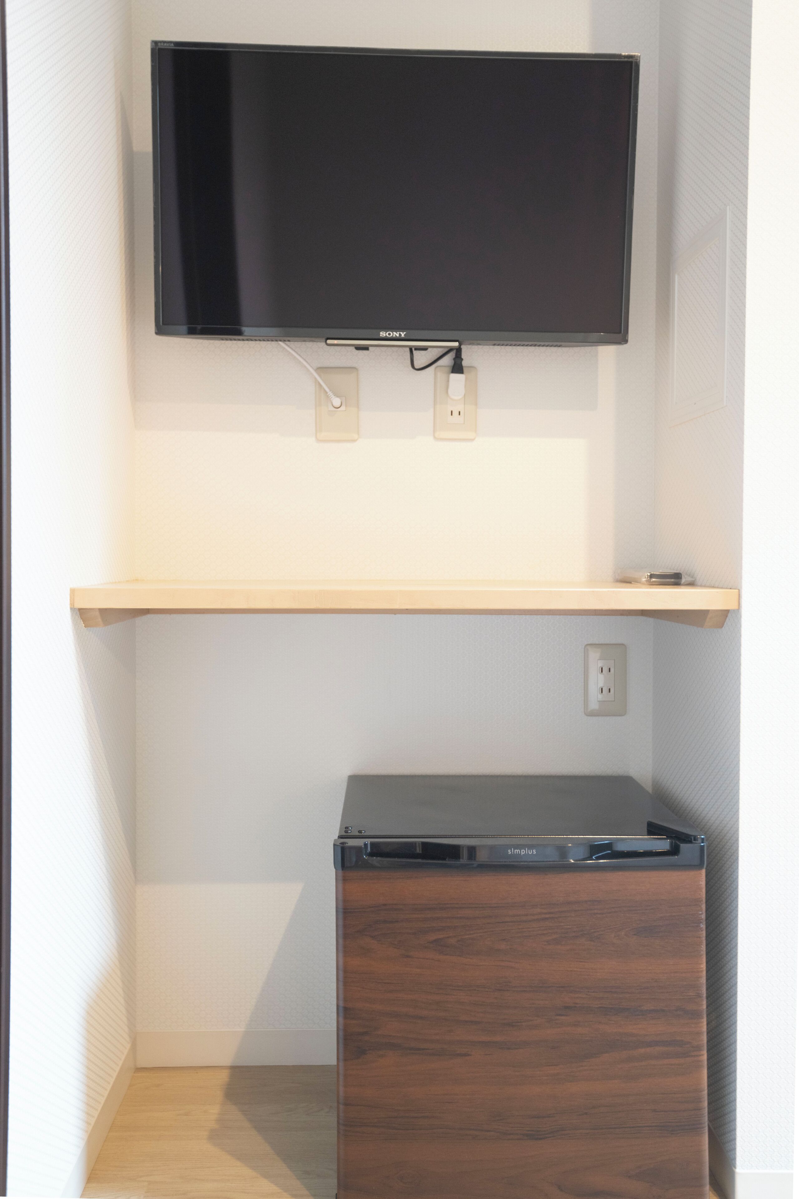 A flat-screen TV mounted on a wall above a wooden shelf.