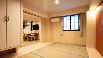 A room with tatami flooring, a sliding door, a window with curtains, and a kitchenette in the background.
