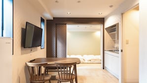 A modern hotel room with a dining area, a TV mounted on the wall, and a kitchenette. - Tokyo Biyori Hotel (Tokyo)