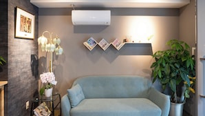 A modern living room with a sofa, a potted plant, and a wall-mounted air conditioner. - Tokyo Biyori Hotel (Tokyo)