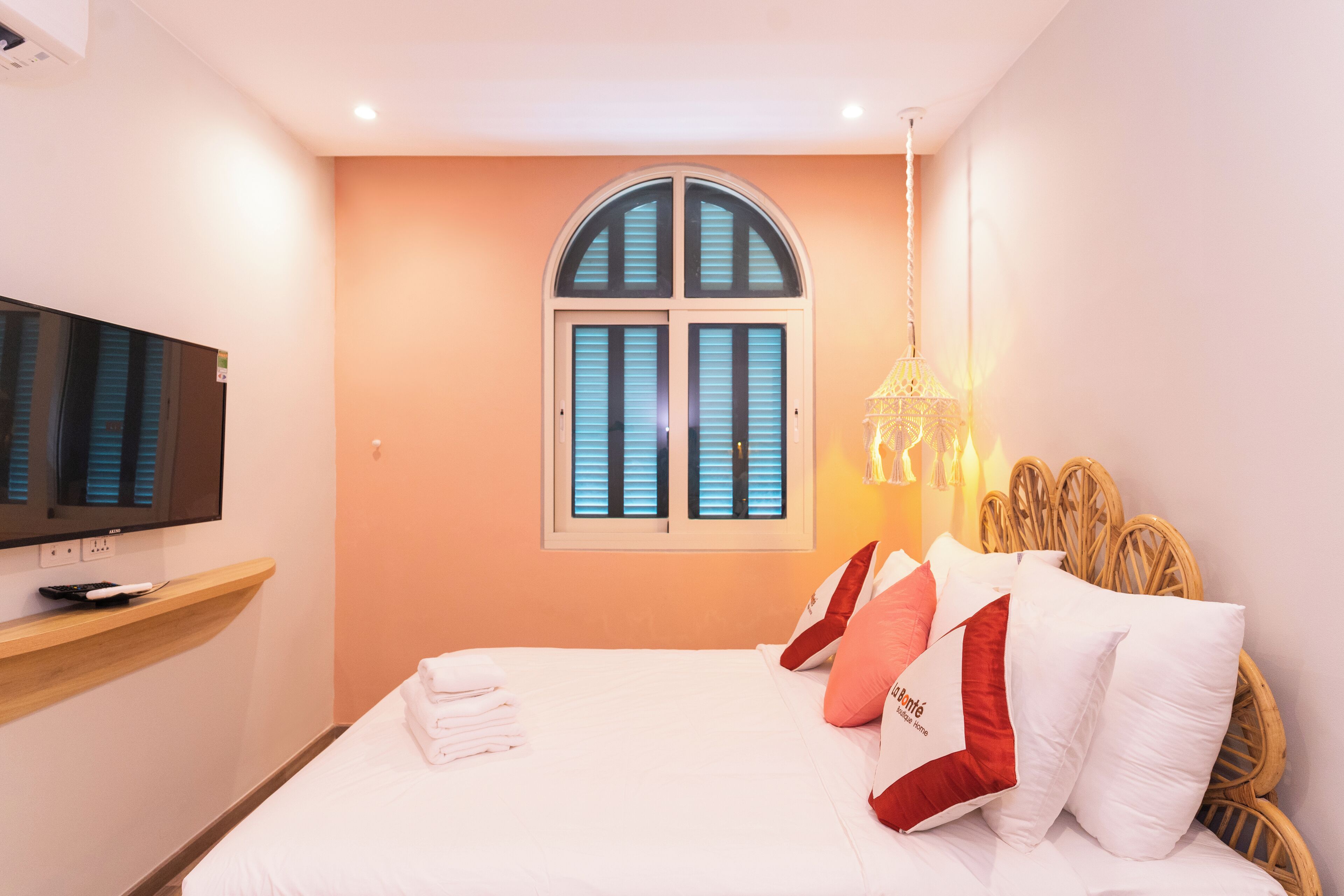 Una habitación de hotel con cama, televisión, ventana con contraventanas y lámpara colgante.