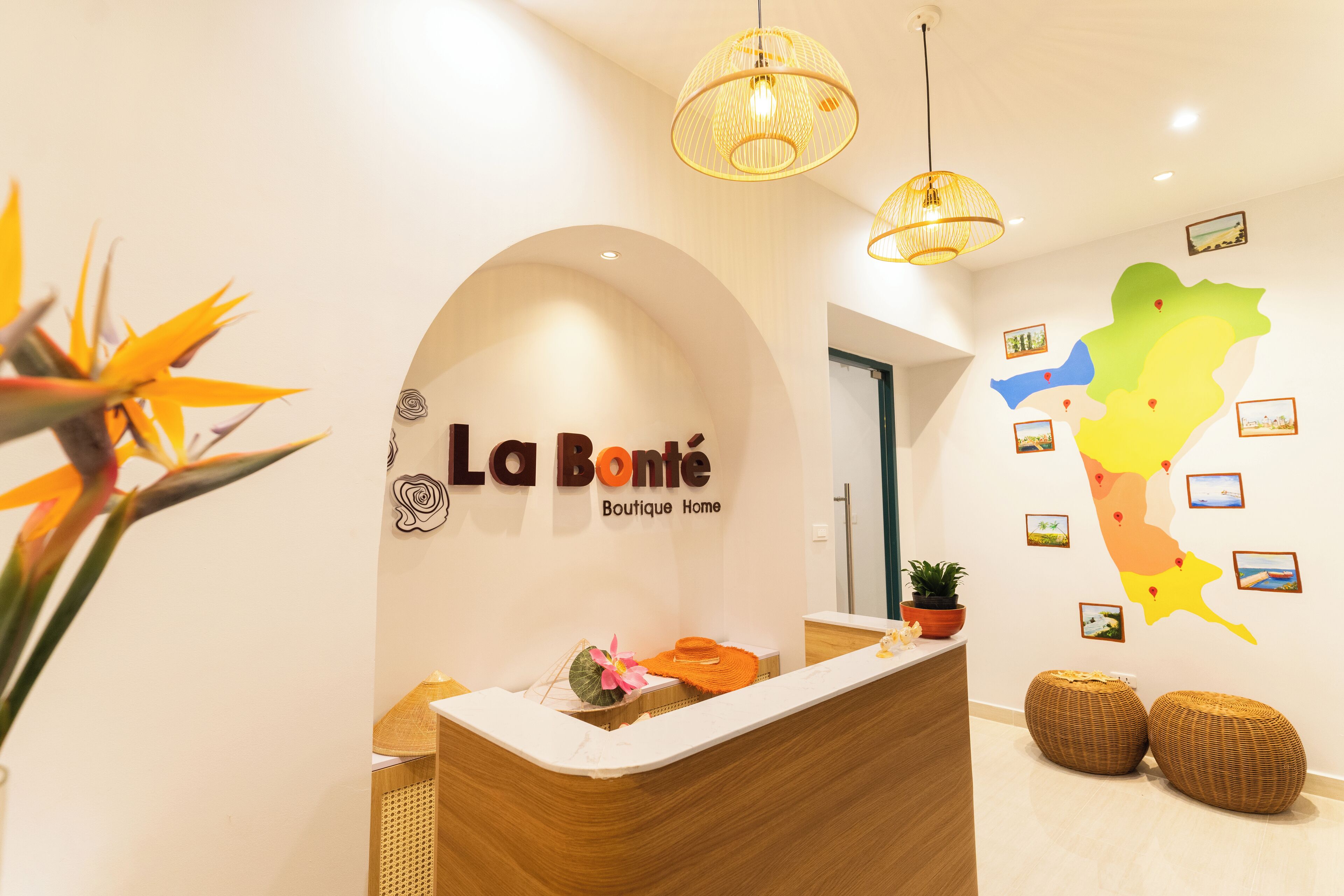 A reception area with a sign reading 'La Bonte Boutique Home,' a reception desk, wicker ottomans, and a wall with a map and photos.