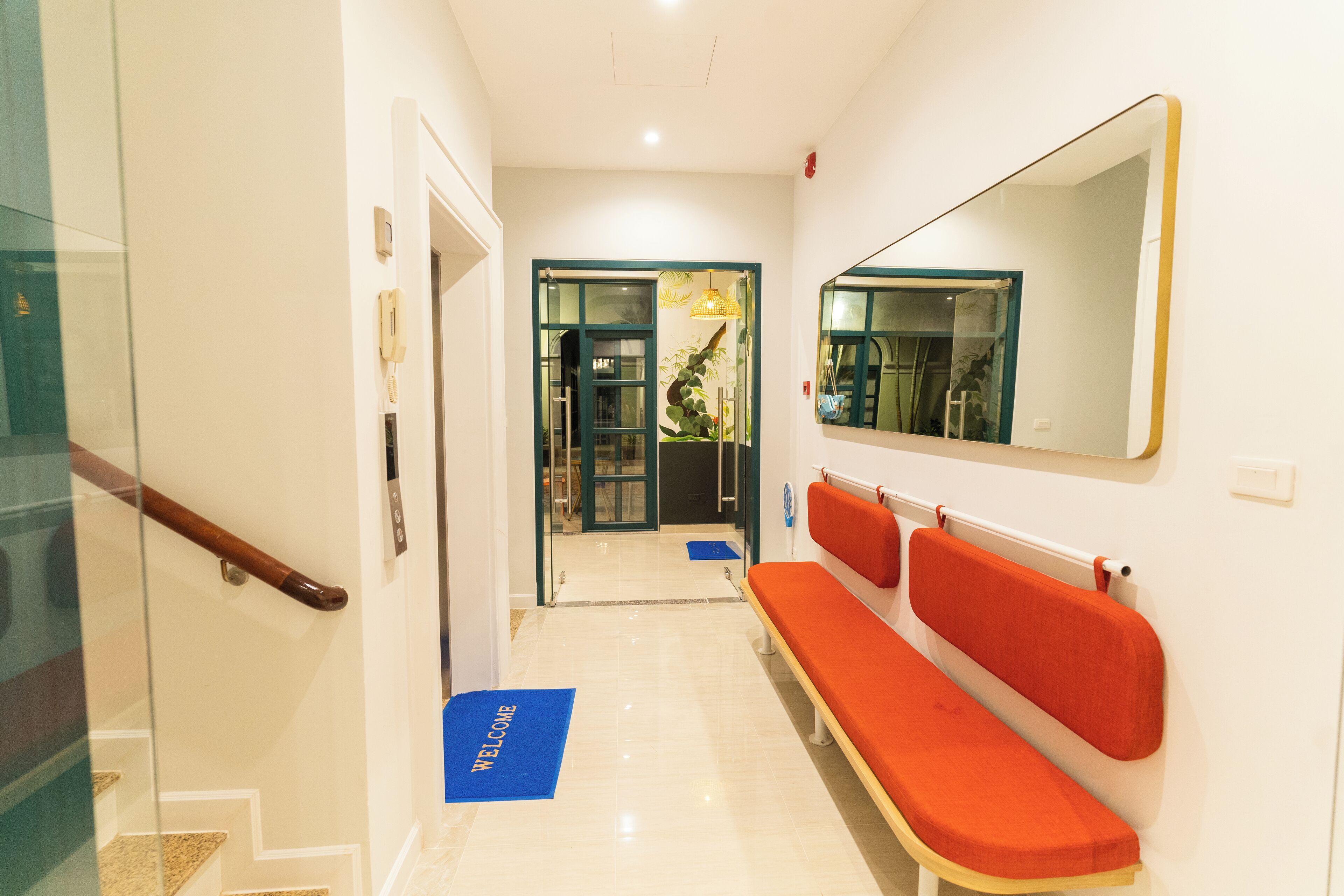 A hotel lobby with a reception desk, a bench, a mirror, and a staircase.