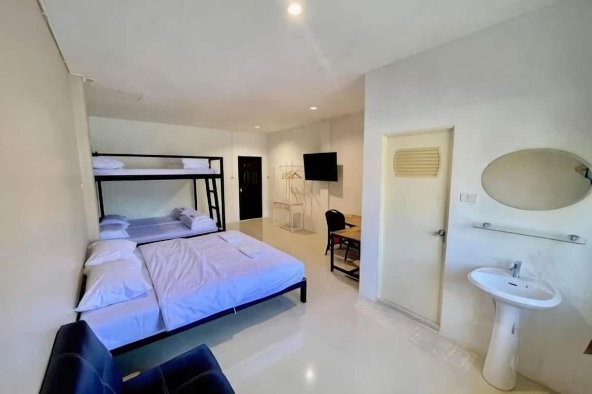 Ein Hotelzimmer mit Etagenbetten, einem Schreibtisch, einem Stuhl, einem Fernseher und einem Badezimmer mit Waschbecken und Spiegel.