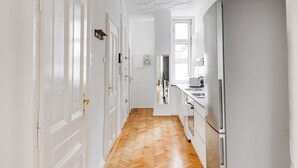 A hallway with white doors, a wooden floor, and a kitchen area with a refrigerator and sink.