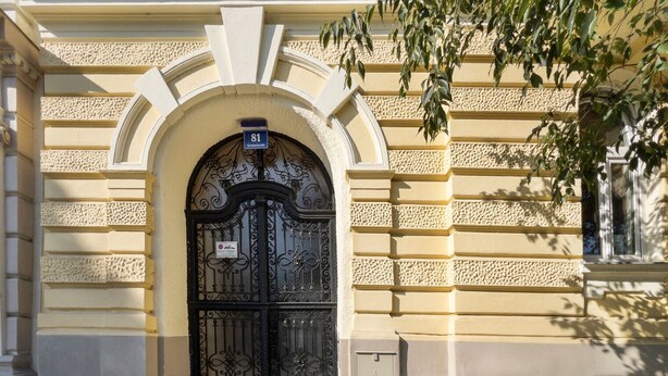 A building entrance with a black ornate gate, a sign above the door, and a utility box to the right.