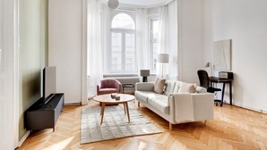 A modern living room with a sofa, armchair, and coffee table, a TV, and a desk with a lamp.