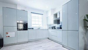 Una cucina moderna con mobili bianchi, forno integrato e una finestra con persiane.