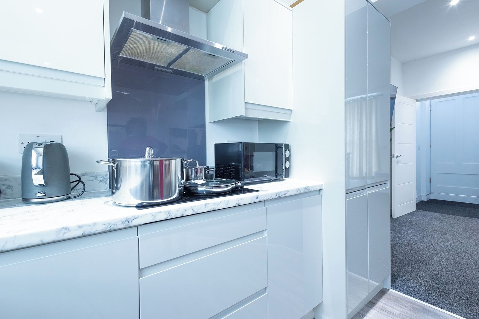 A modern kitchen with white cabinets, a stainless steel kettle, a pot, a microwave, and a stove.