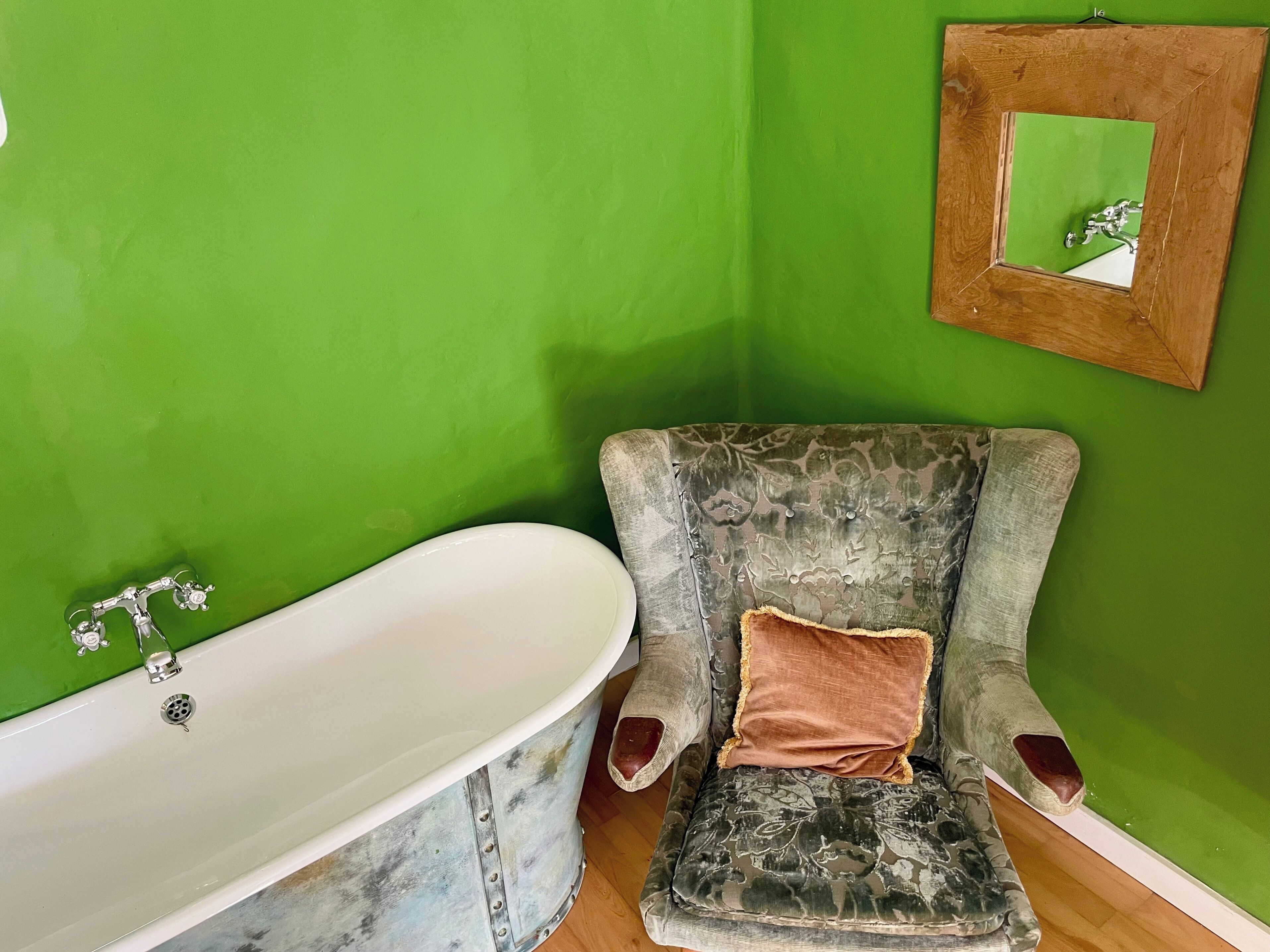 A bathroom with a white bathtub, a floral-patterned armchair, and a green wall.
