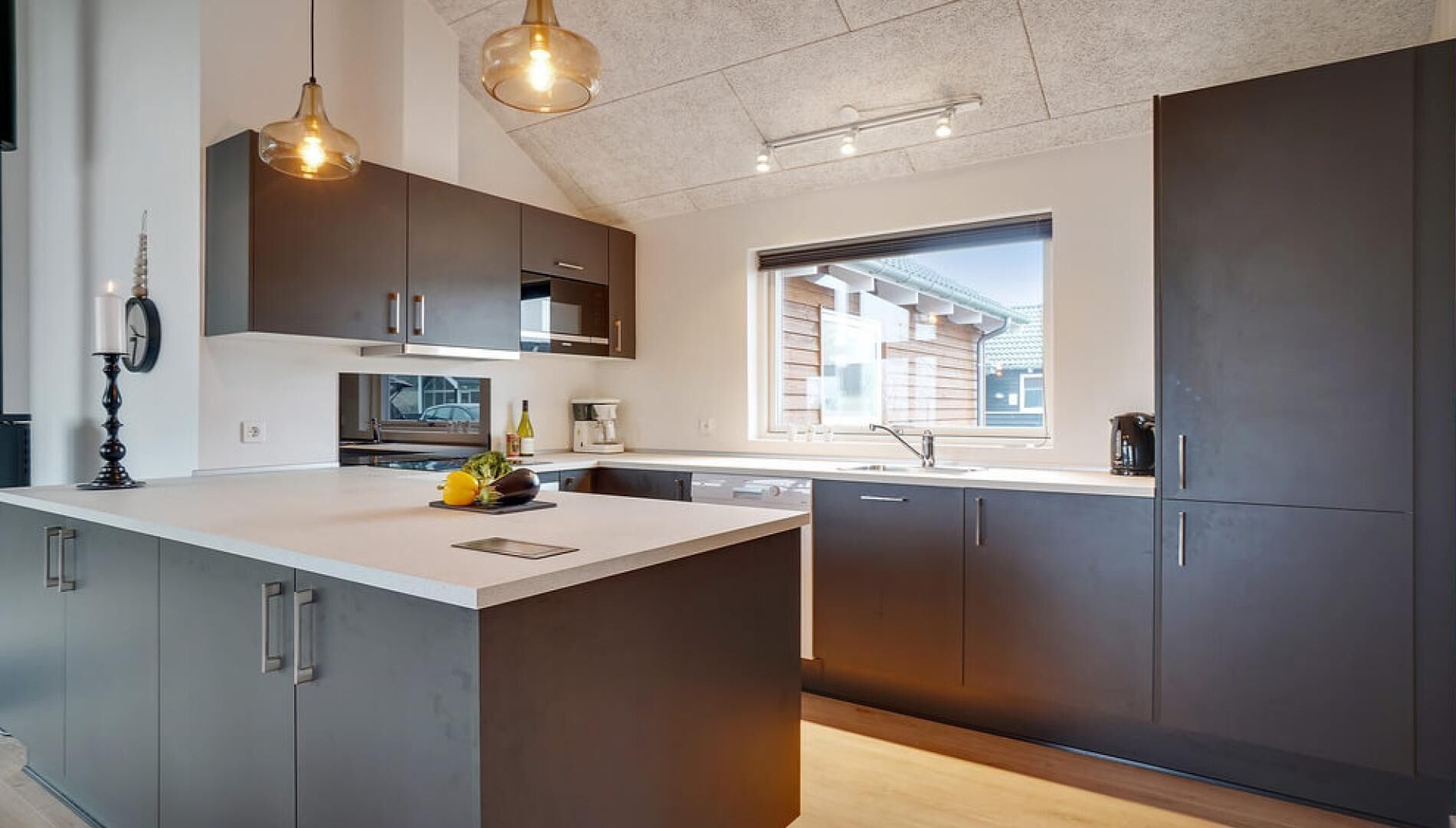 A modern kitchen with a large island, dark cabinetry, and pendant lighting.