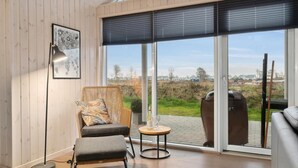 Ein modernes Zimmer mit einem großen Fenster, einem Korbstuhl, einem kleinen runden Tisch und einem Sofa.