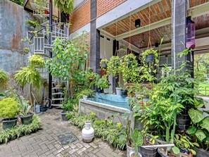 A courtyard with various potted plants, a white vase, and a staircase leading to a balcony. - Huiz de RiCo guesthouse syariah (Yogyakarta)