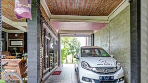 Un coche blanco estacionado en un camino de entrada cubierto, con suelo de baldosas y techo de madera.