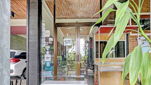 Un restaurante con puerta de cristal, una banca blanca en el exterior y un coche estacionado cerca.