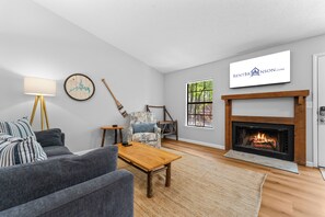 Una sala de estar con chimenea, televisor montado y comedor.