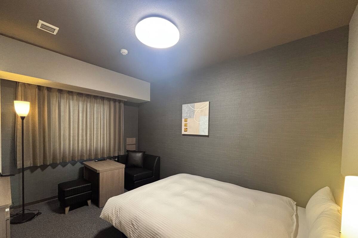 Une chambre d’hôtel avec un grand lit, un bureau, une chaise, une lampe et un tableau au mur.