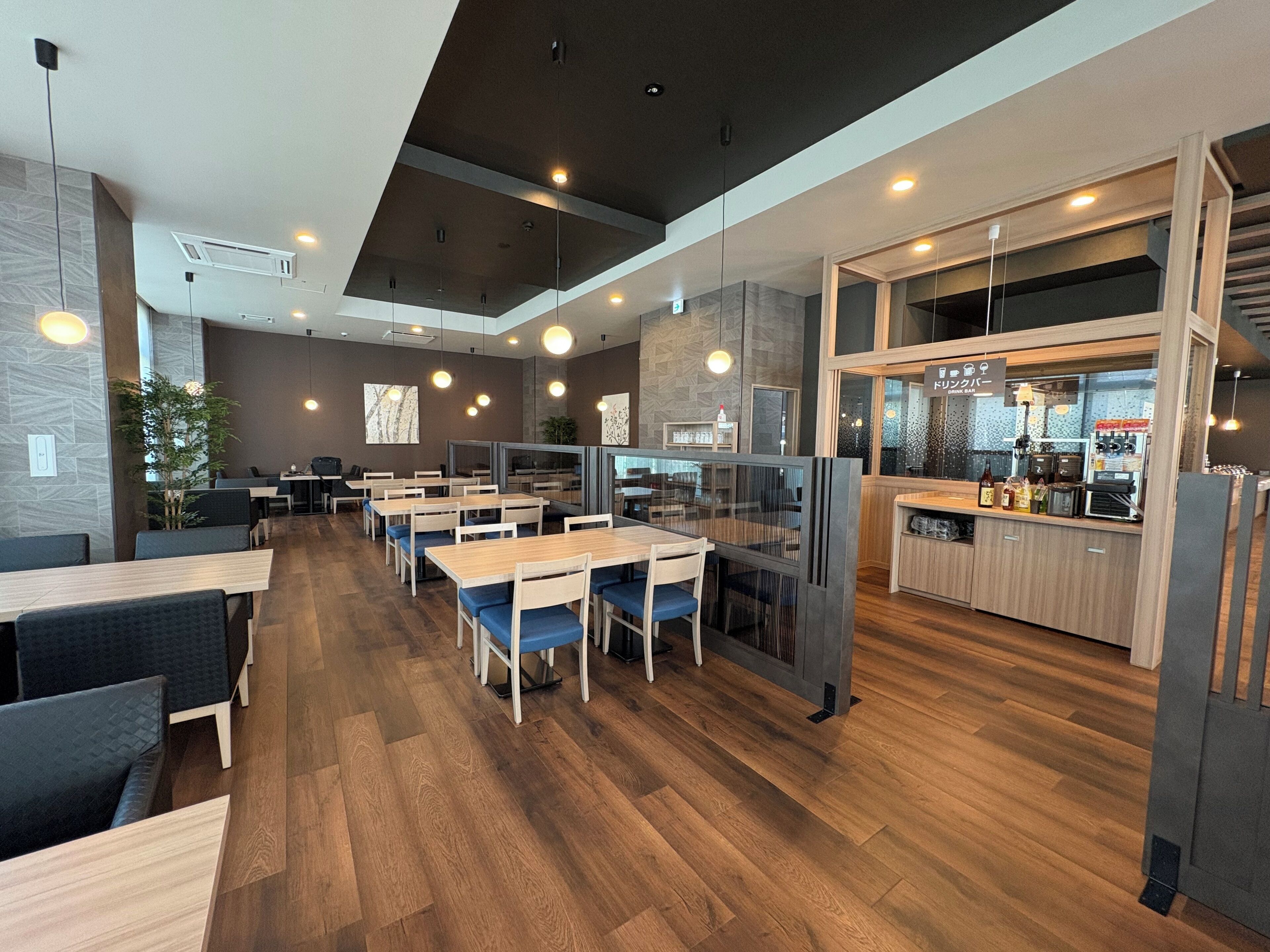 A modern restaurant with multiple dining areas, a bar, and a kitchen visible through a glass partition.