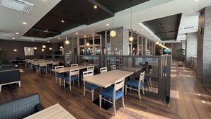 Un restaurante moderno con mesas de madera y sillas acolchadas en azul, un entrepiso y una escalera que conduce al piso superior.