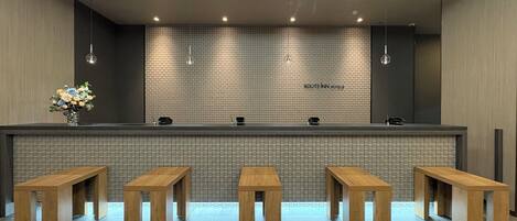 Un área de recepción con una pared de azulejos, un mostrador y bancos de madera.