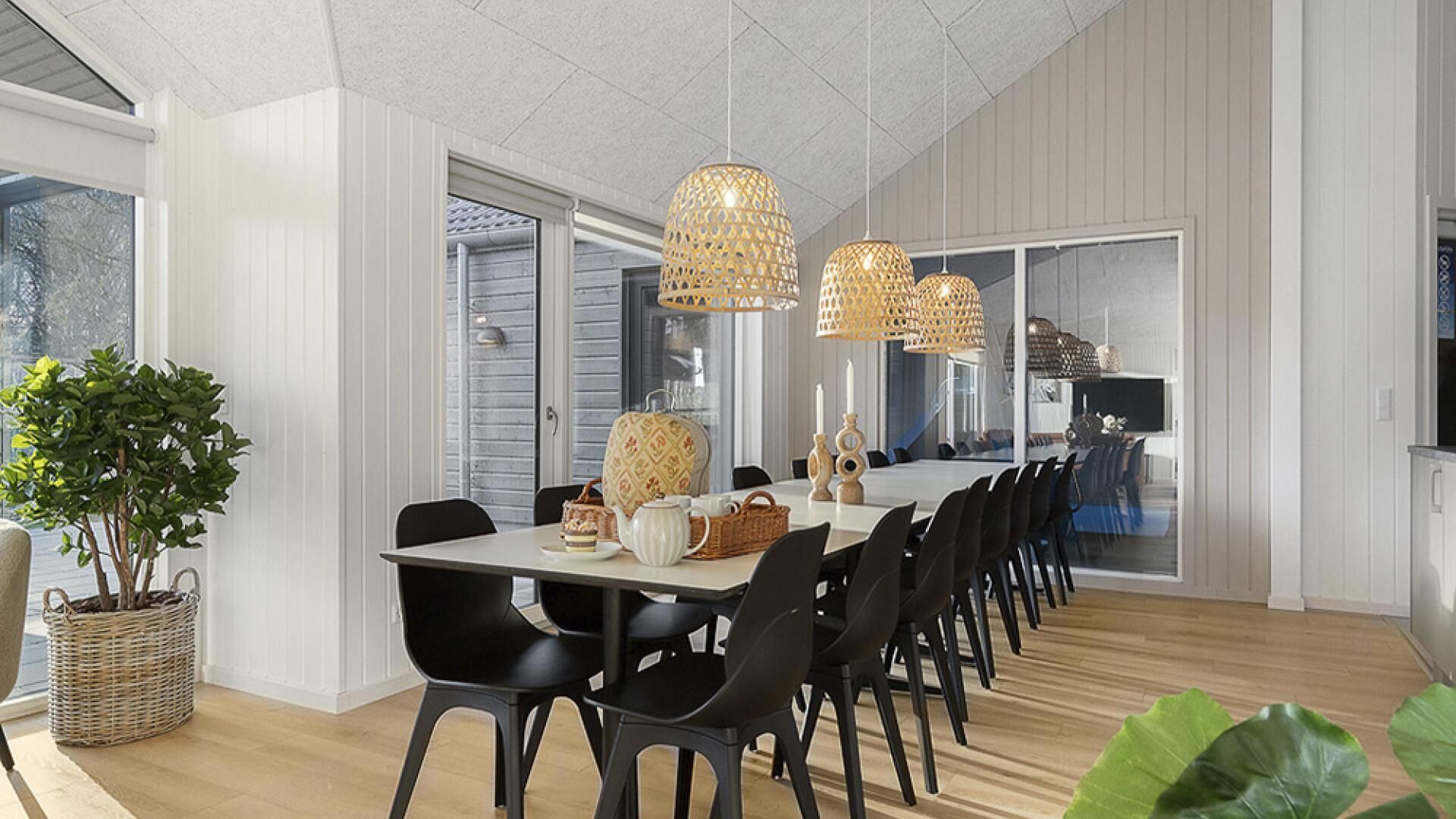 A modern dining area with a long table, black chairs, wicker baskets, and a potted plant.