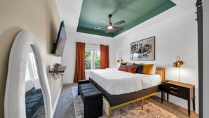 A bedroom with a bed, bedside tables, a ceiling fan, a wall-mounted TV, and a window with curtains. - Houston Getaway I Near NRG, Downtown, Airport (Houston)