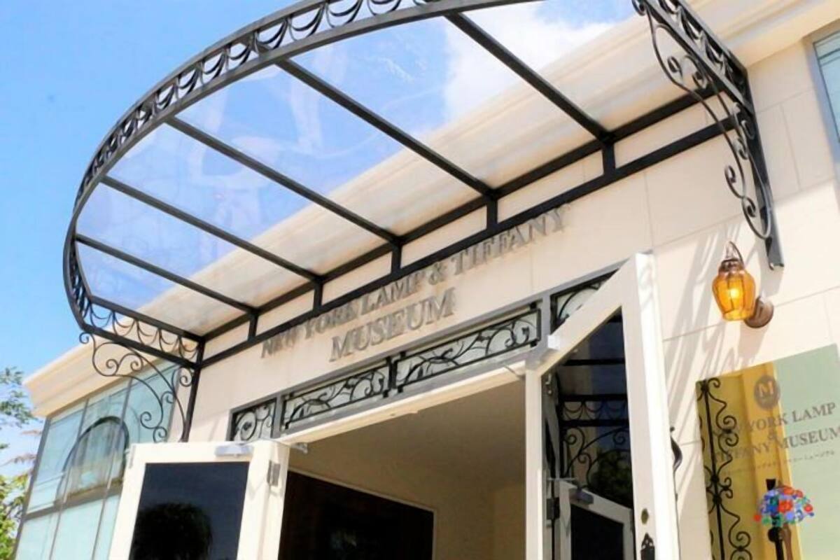 The entrance to the New York Lamplight & Tiffany Museum with a glass canopy and decorative metalwork.