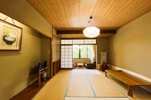 Egy hagyományos japán szoba, tatamiszőnyeggel borított padlóval, fa mennyezettel és egy alacsony állványon elhelyezett televízióval.
