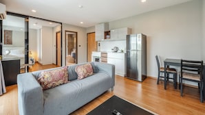 A modern living room with a grey sofa, a dining table with chairs, a kitchen area with white cabinets and a stainless steel refrigerator. - Modern Condo Walk to Rawai Beach C188 (Rawai)